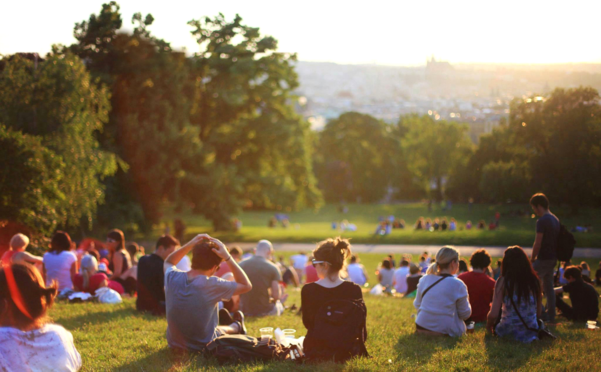 De nombreuses personnes installées sur la pelouse d'un parc en fin de journée.
