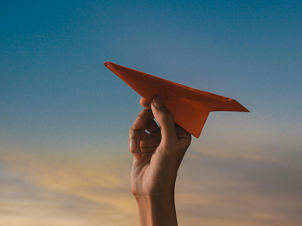 Une main de femme sur le point de lancer un avion en papier orange dans les airs.